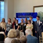 A large contingent of students, faculty and administrators from the South Carolina Governor's School of Science and Math stand in front of the display and room to pose for a group photo at the 2025 Meet the Finalists