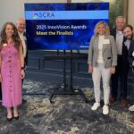 The South Carolina Research Authority - SCRA - presenting sponsor presentation team stands around a TV displaying the title slide of the Meet the Finalists event of the 2025 InnoVision Awards
