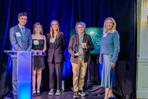 Members of the Robotics Program at the SC Governor's School for Science + Mathematics stand on stage with presenter Susie Shannon of SC Competes to accept their award for Community Service at the 2025 InnoVision Awards